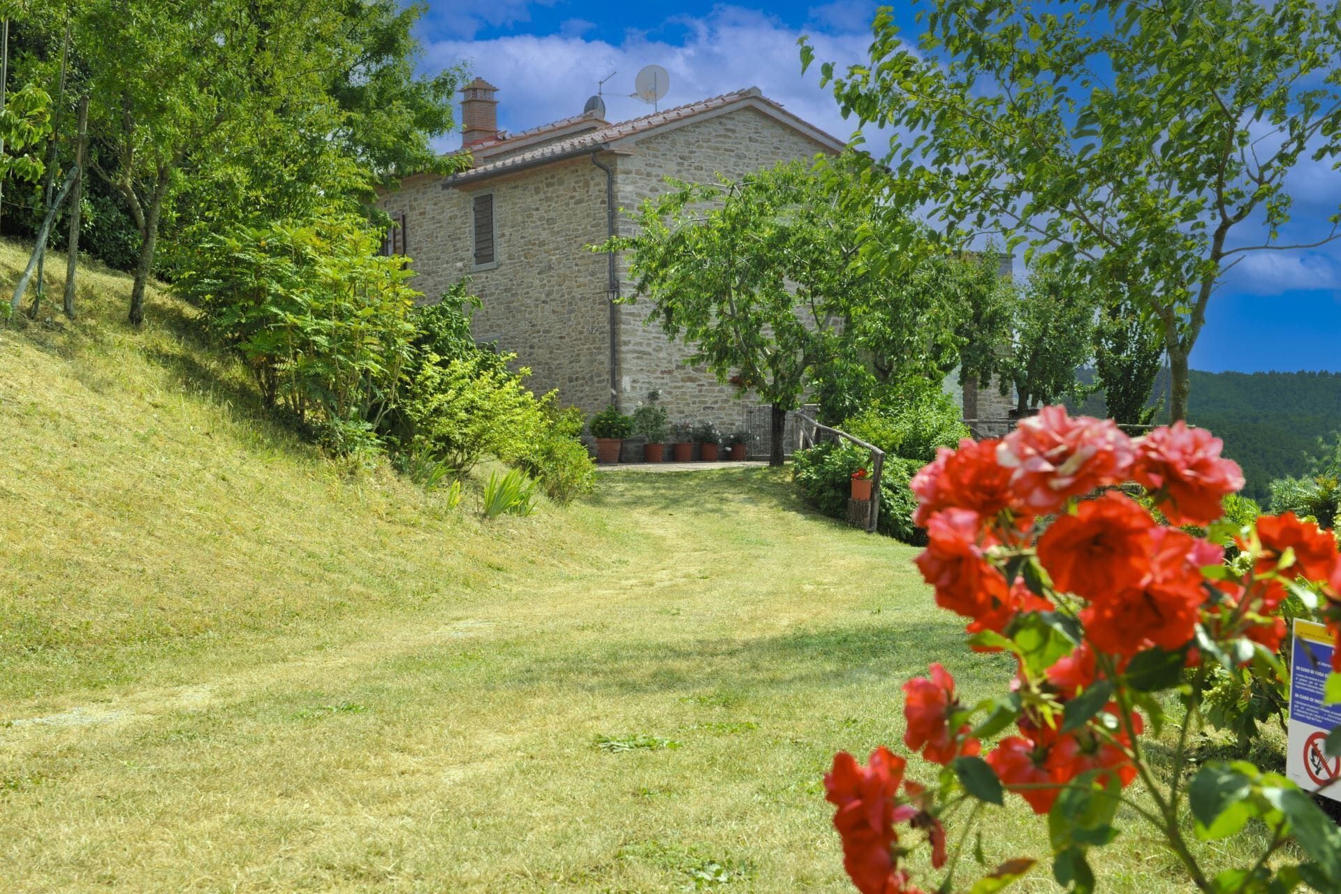 Un bâtiment en pierre doté d’un toit en pente, entouré de verdure et d’une zone herbeuse.