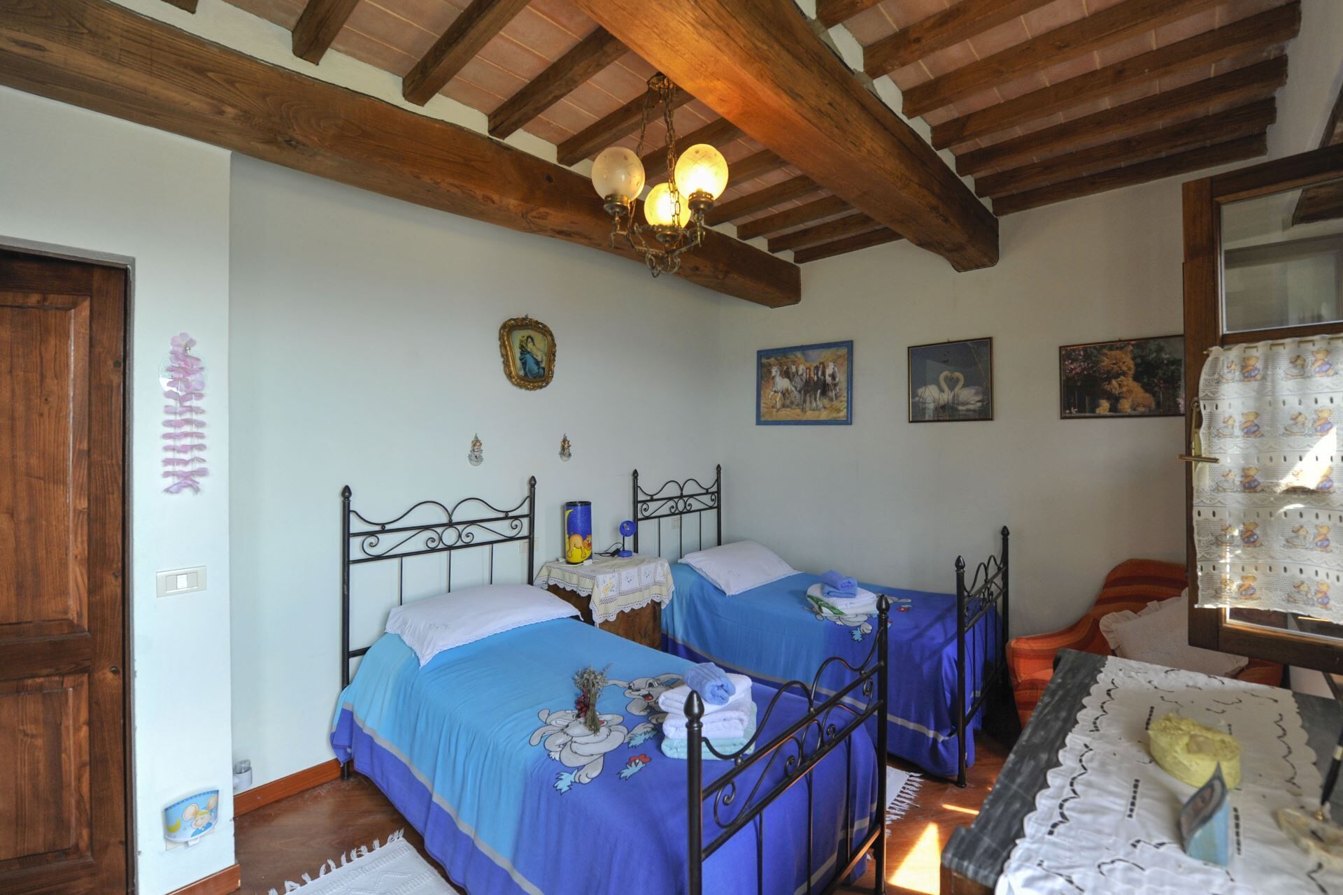 Une chambre avec deux lits, des poutres en bois, un lustre et des œuvres d’art murales.