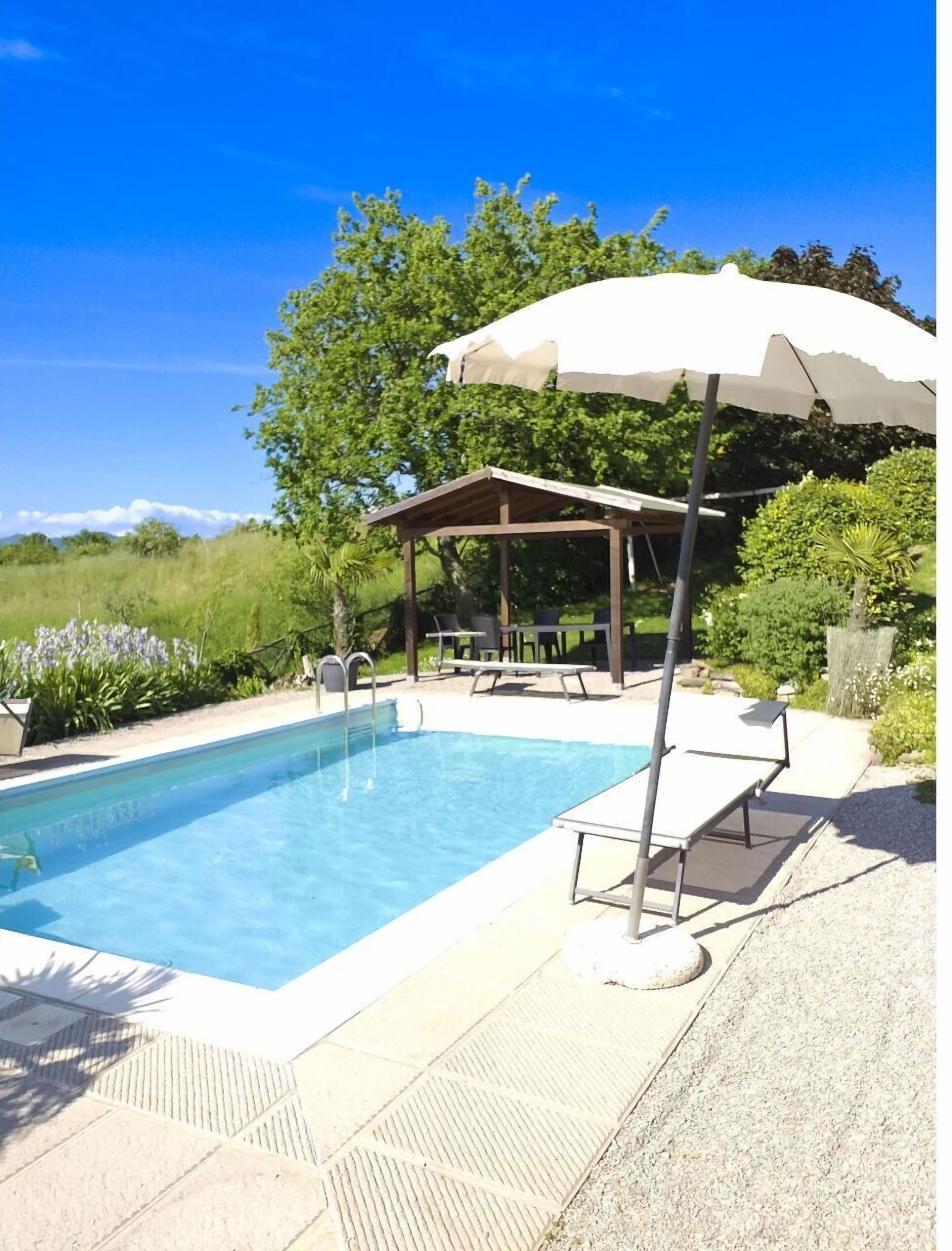 A swimming pool with a covered seating area, lounge chairs, and a pergola with an umbrella.