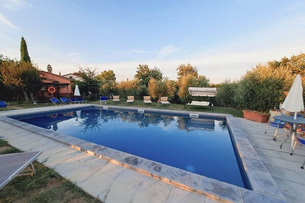 A rectangular swimming pool with a tiled edge, surrounded by lounge chairs and umbrellas.