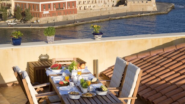 Una terrazza con un tavolo apparecchiato per mangiare, vista su uno specchio d'acqua e edifici.