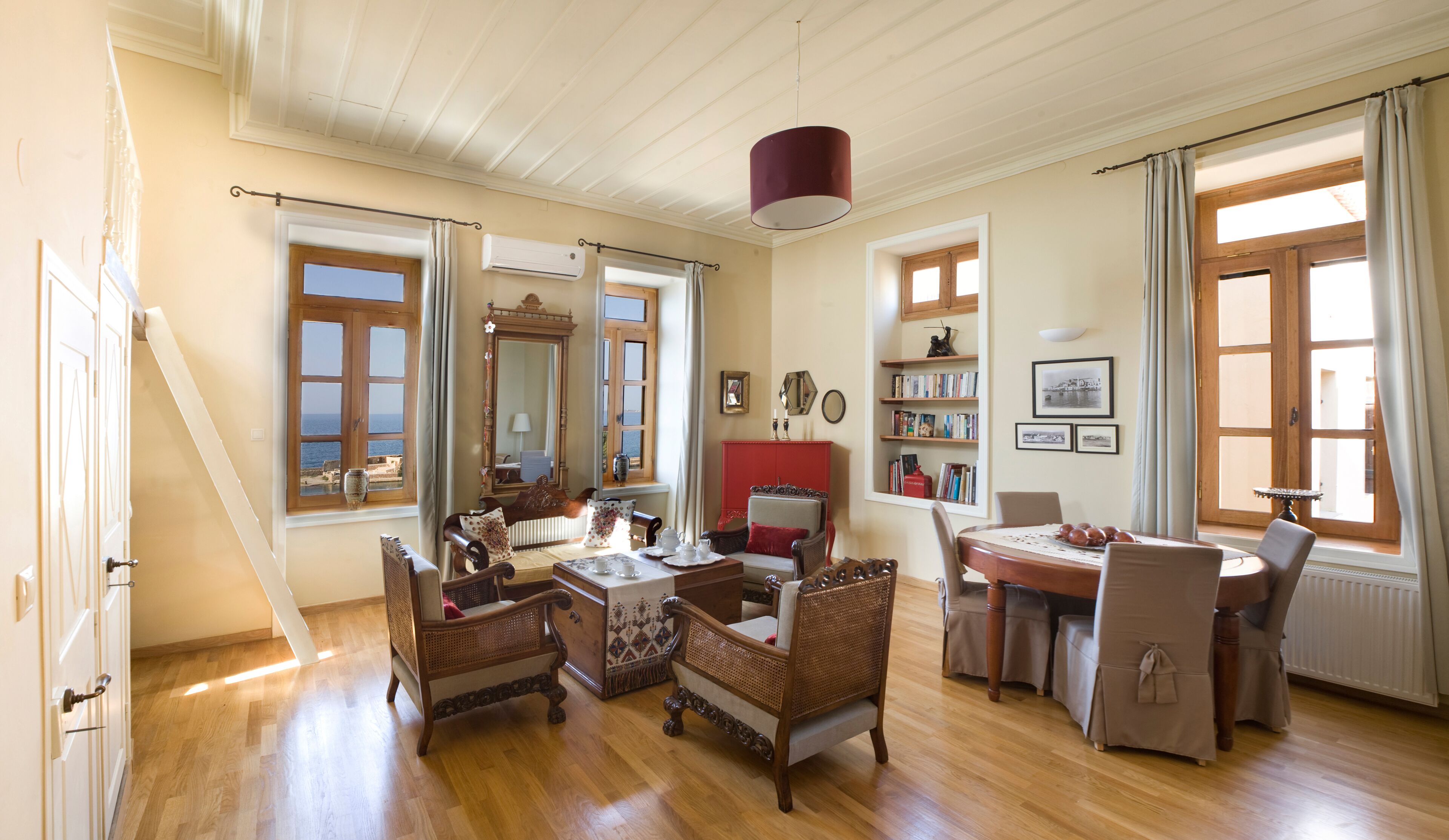 Une pièce spacieuse avec un plancher en bois, un coin repas comprenant une table et des chaises, un buffet rouge et une grande fenêtre donnant sur un beau paysage.