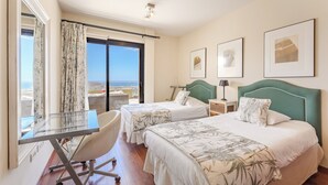 Ett hotellrum med två sängar, ett skrivbord och utsikt över havet.