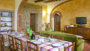 Un comedor con una mesa dispuesta para cuatro personas, un sofá verde y un televisor sobre un mueble de madera.