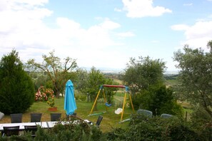 Enjoy a serene garden with a swing set and dining area, surrounded by a lush landscape offering panoramic views of the countryside.