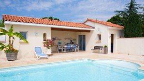A swimming pool with a tiled deck, a covered patio area with a table and chairs, and a potted plant. - Country Cottage / Gite - LOUBERS (Loubers)
