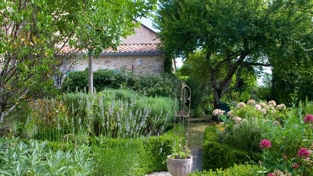 A garden with a stone pathway, various plants, and a building with a tiled roof in the background. - Country Cottage / Gite - LOUBERS (Loubers)