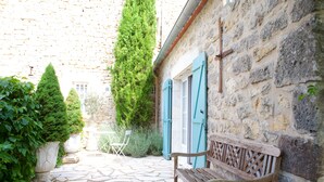 A stone-paved courtyard with a wooden bench, a chair, and a building with blue shutters. - Country Cottage / Gite - LOUBERS (Loubers)