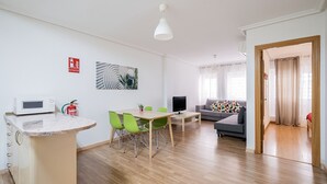 A modern living room with a dining area, a sofa, a television, and a kitchen area with a microwave. - Downtown Madrid North Barrio del Pilar. Tempory (Madrid)
