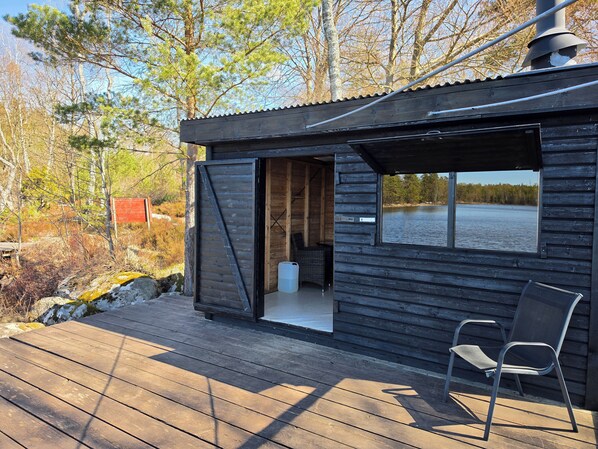 A cabin with a deck, a chair, and a window overlooking a body of water. - Cozy cottage near the lake, including free Wi-Fi and own rowing boat (Hallaryd)