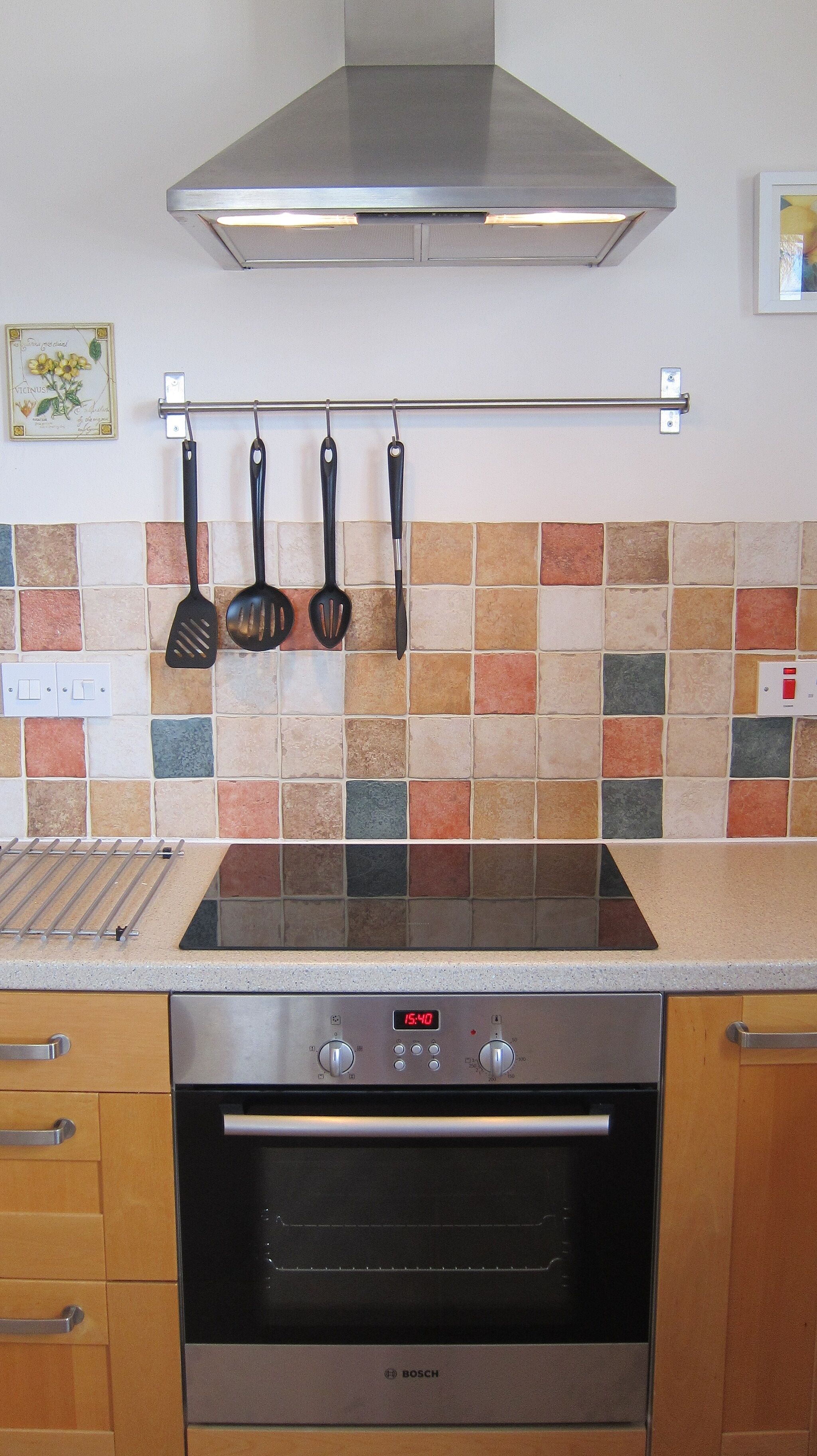 A kitchen with a Bosch oven, a tiled backsplash, and hanging utensils.