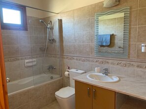 Une salle de bain équipée d’une baignoire, d’une douche, de toilettes, d’un lavabo et d’un miroir sur lequel est accrochée une serviette.