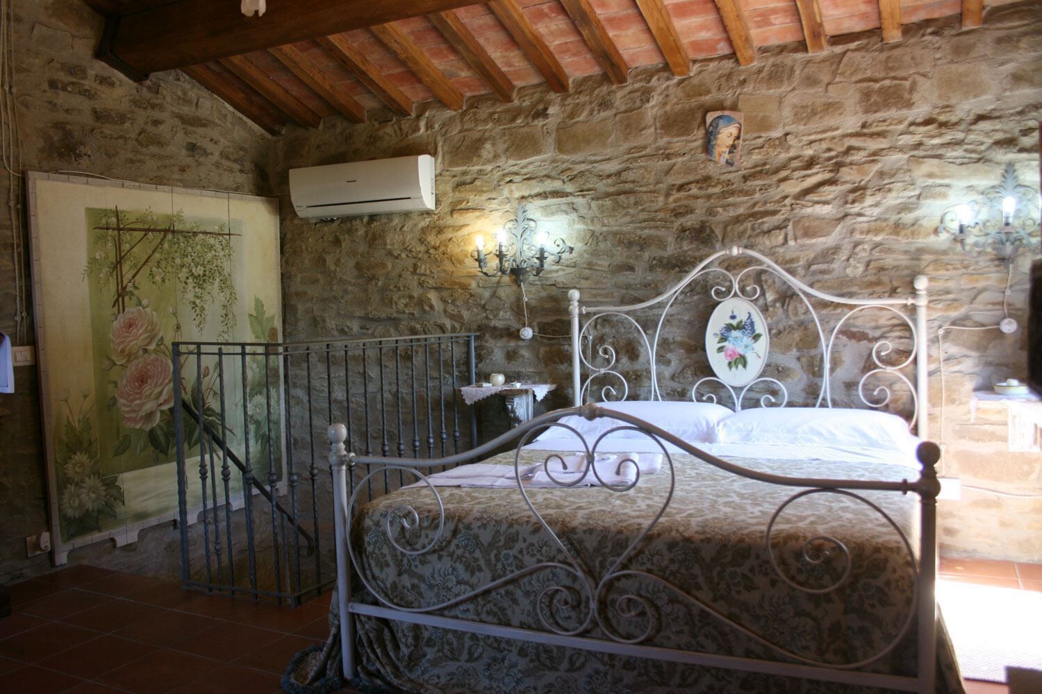 Un dormitorio con pared de piedra, estructura de cama metálica y unidad de aire acondicionado.