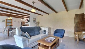 Ein Wohnzimmer mit einer Couch, einem Couchtisch und einem Sessel. Im Hintergrund ist ein Essbereich mit Tisch und Stühlen zu sehen.