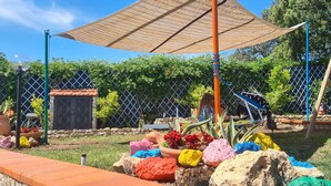 A playground with a swing set, climbing structure, and a fenced area with colorful rocks and plants. - L'ULIVETA DEL LUSCHI VILLA, PISCINA  E CAMPO DA TENNIS, WI-FI, PET FRIENDLY (ROSIGNANO MARITTIMO)