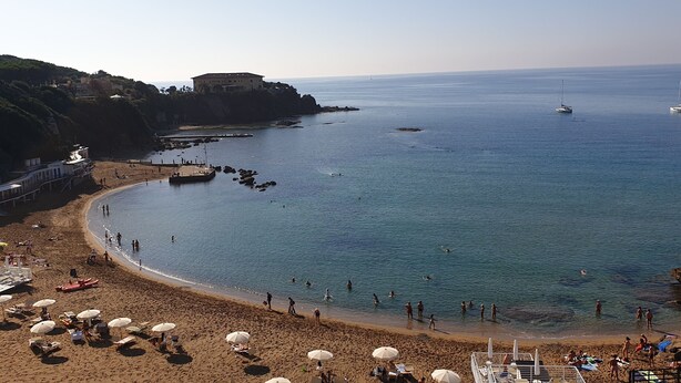 A beach with people, boats, and a building on a cliff. - L'ULIVETA DEL LUSCHI VILLA, PISCINA  E CAMPO DA TENNIS, WI-FI, PET FRIENDLY (ROSIGNANO MARITTIMO)