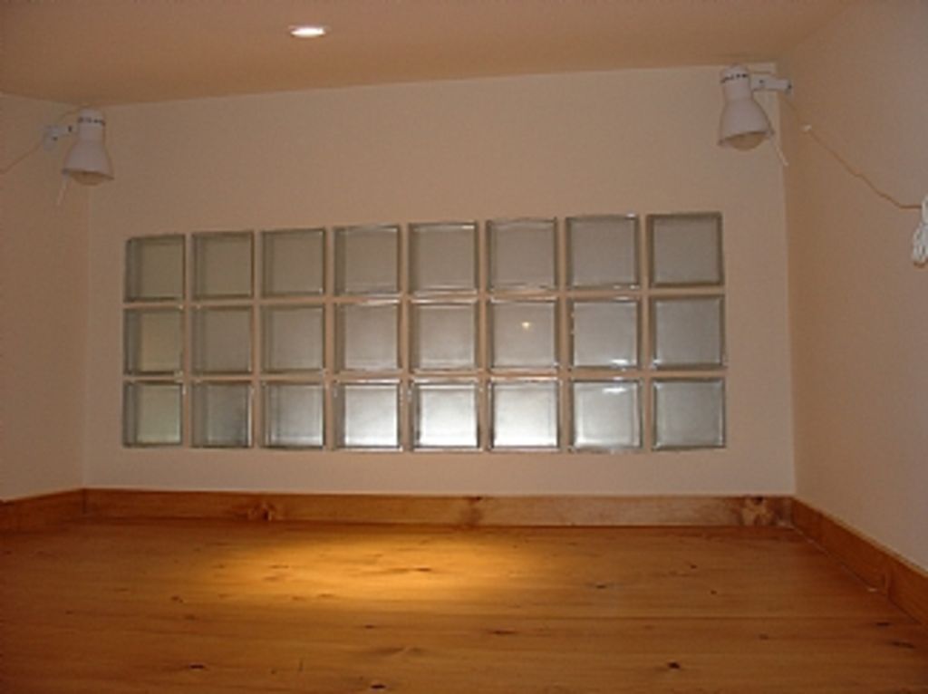 A room with a large window, wooden flooring, and two wall-mounted lamps.