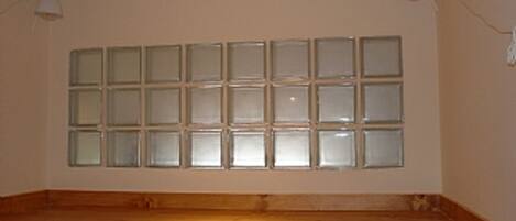 A room with a large window, wooden flooring, and two wall-mounted lamps.