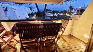 Un balcón con mesa y sillas, con vistas a una zona costera con edificios y palmeras.