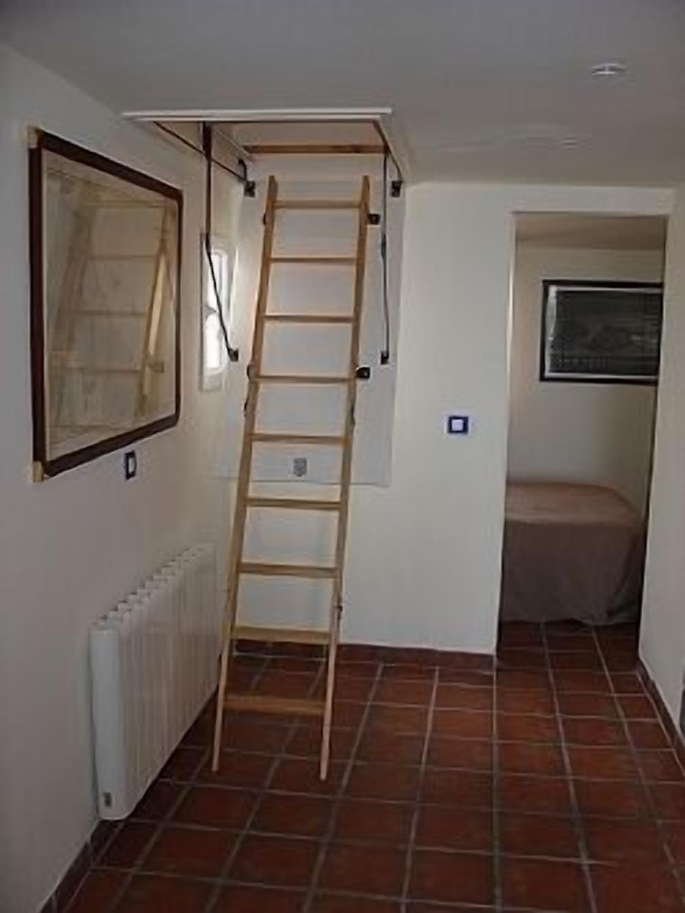 A narrow hallway with a wooden ladder leading to an upper level, a radiator on the left, and a window with a curtain on the right.