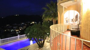 Un balcon avec une piscine, des palmiers et une vue sur la ville la nuit.