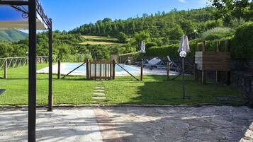 A pool area with a wooden fence, lounge chairs, and a pergola with umbrellas.