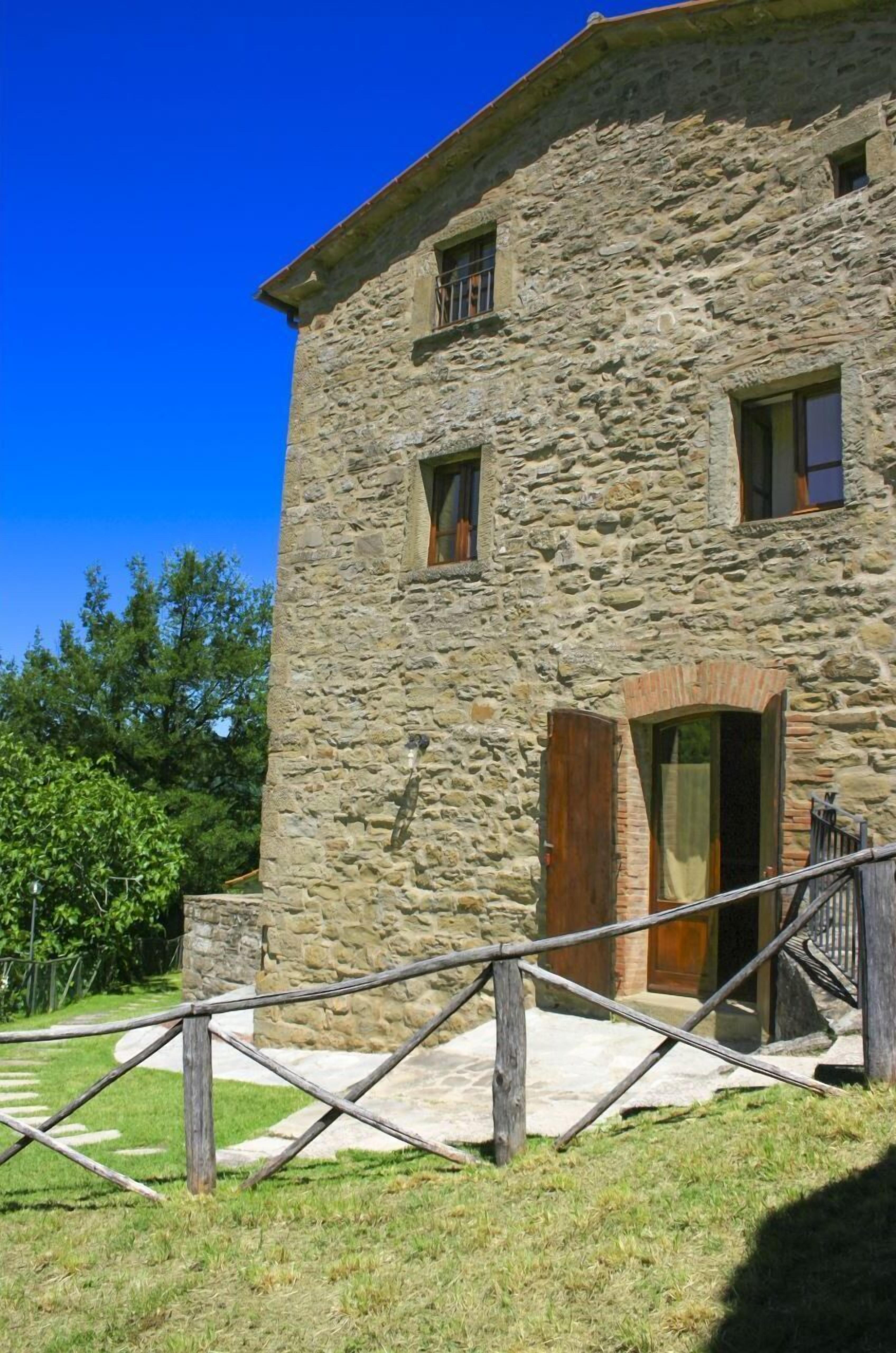 A stone building with a wooden door, a staircase, and a metal railing.