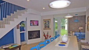 Ein modernes Wohnzimmer mit einem langen Esstisch, blauen Stühlen, einer Treppe, einem Fernseher und einem Kamin.