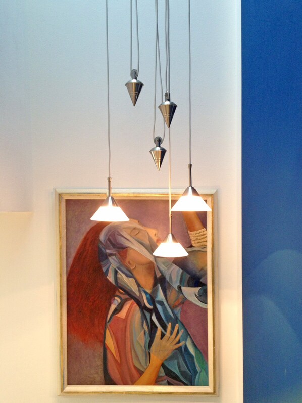 A framed painting with abstract figures and three pendant lights hanging above it.