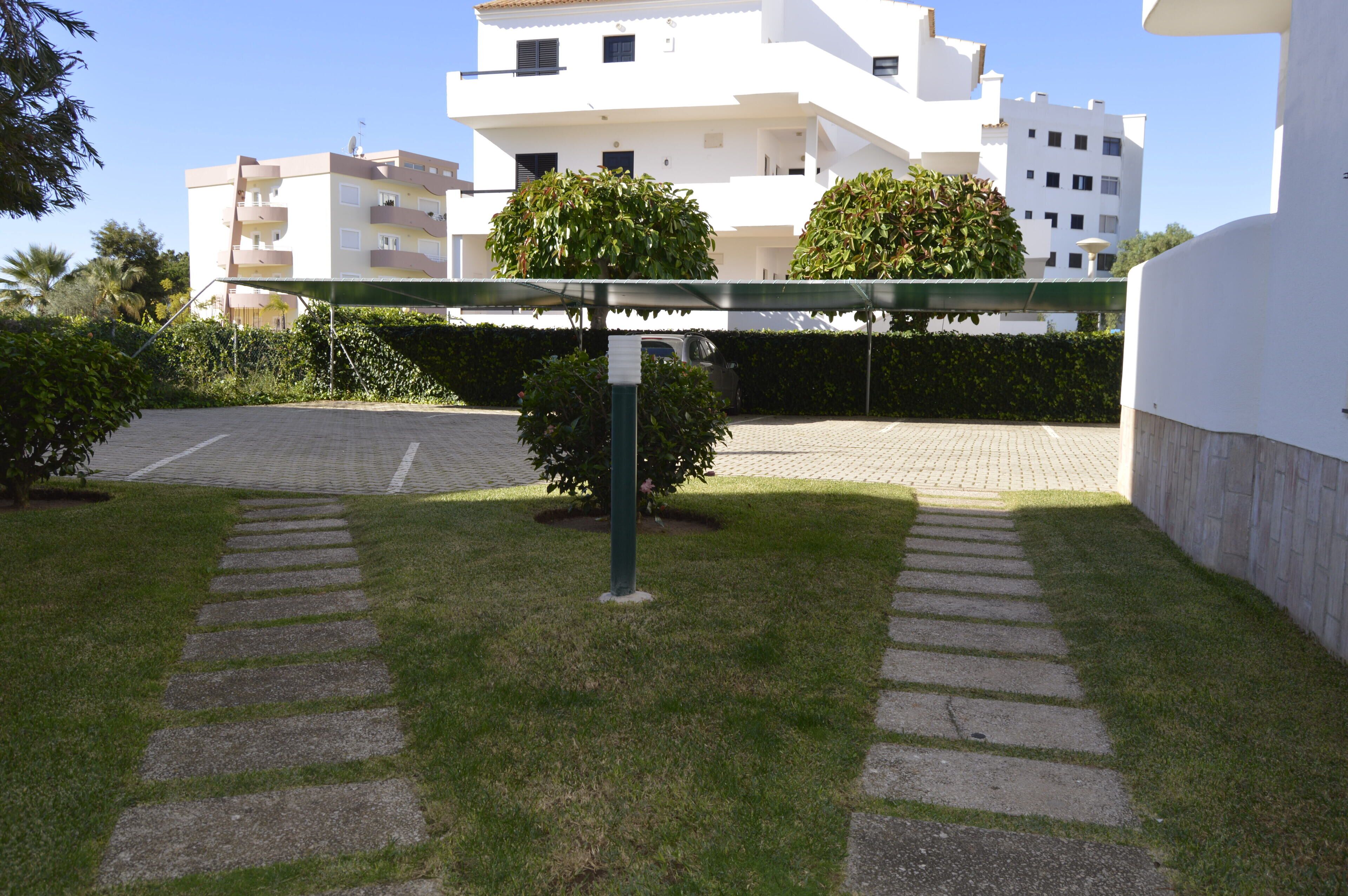 Un camino pavimentado conduce a un estacionamiento cerrado, rodeado de césped y setos bien cuidados bajo un dosel verde.