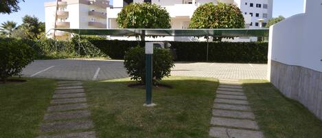 Un camino pavimentado conduce a un estacionamiento cerrado, rodeado de césped y setos bien cuidados bajo un dosel verde.