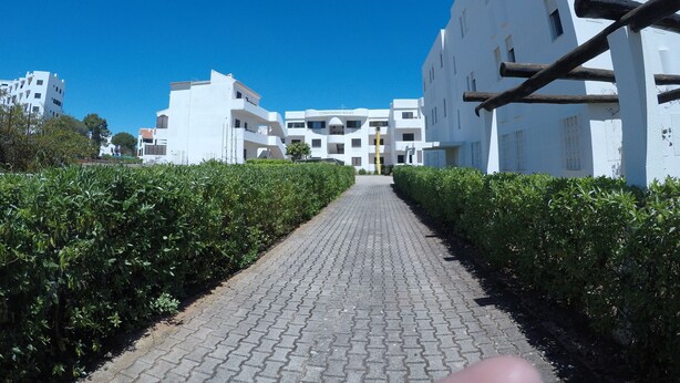 Un chemin mène à un bâtiment blanc doté de balcons, entouré de verdure.