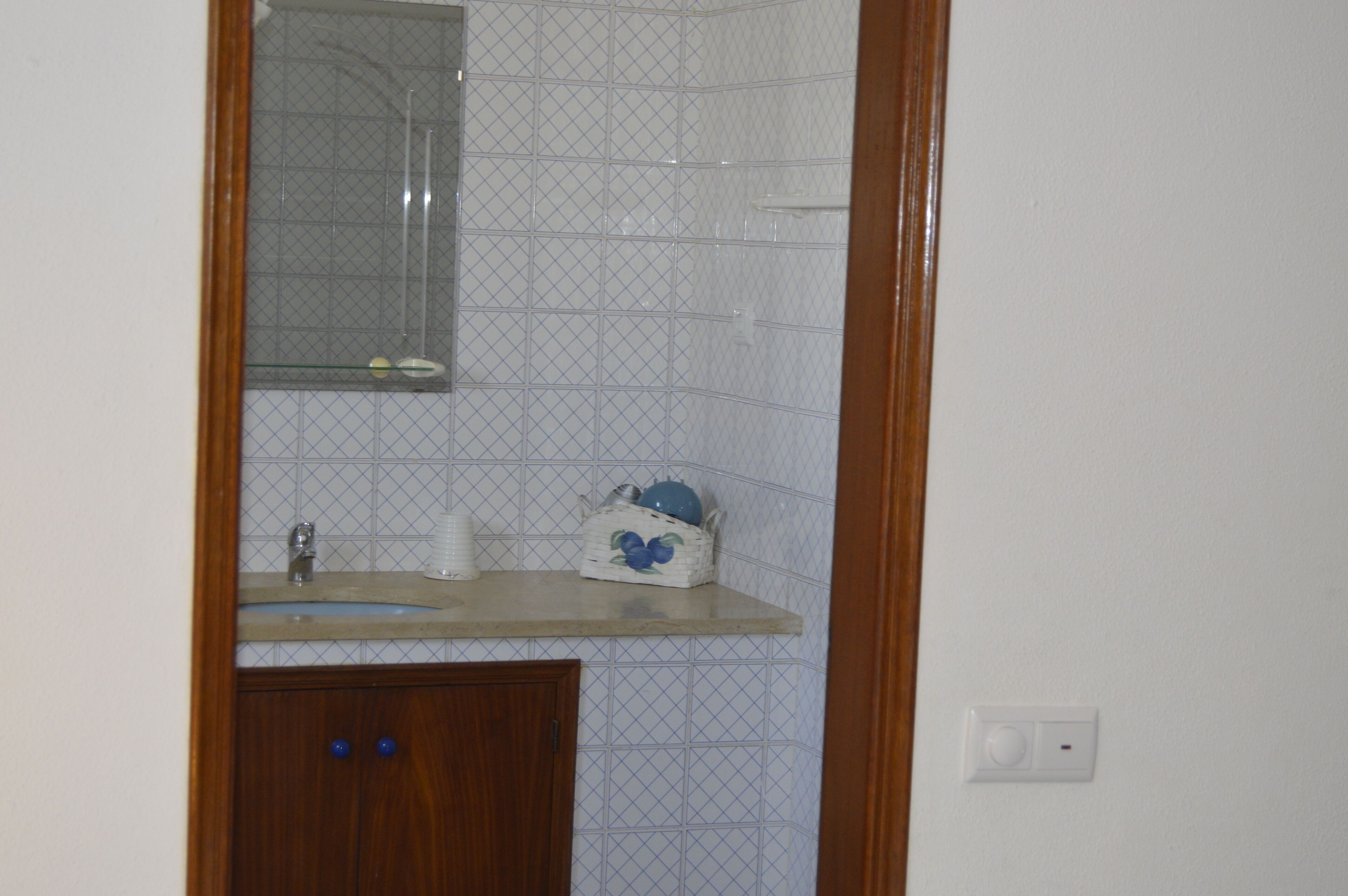 Une salle de bain avec un meuble en bois, un miroir et un lavabo sur lequel est posé un objet décoratif bleu.