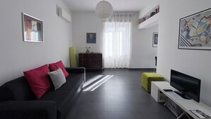 Un salon moderne avec un canapé foncé, un téléviseur à écran plat, une petite table et une bibliothèque.