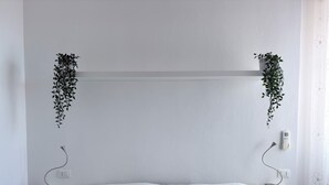 Une chambre à coucher au style minimaliste, avec un lit, des tables de chevet et des plantes suspendues.