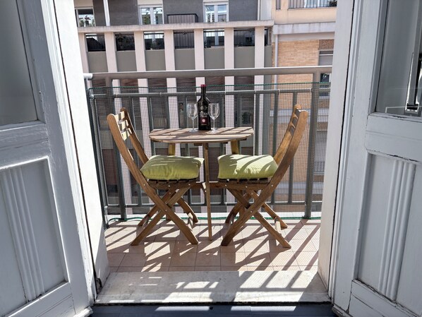 A balcony with a table and two chairs, a bottle of wine, and a glass.