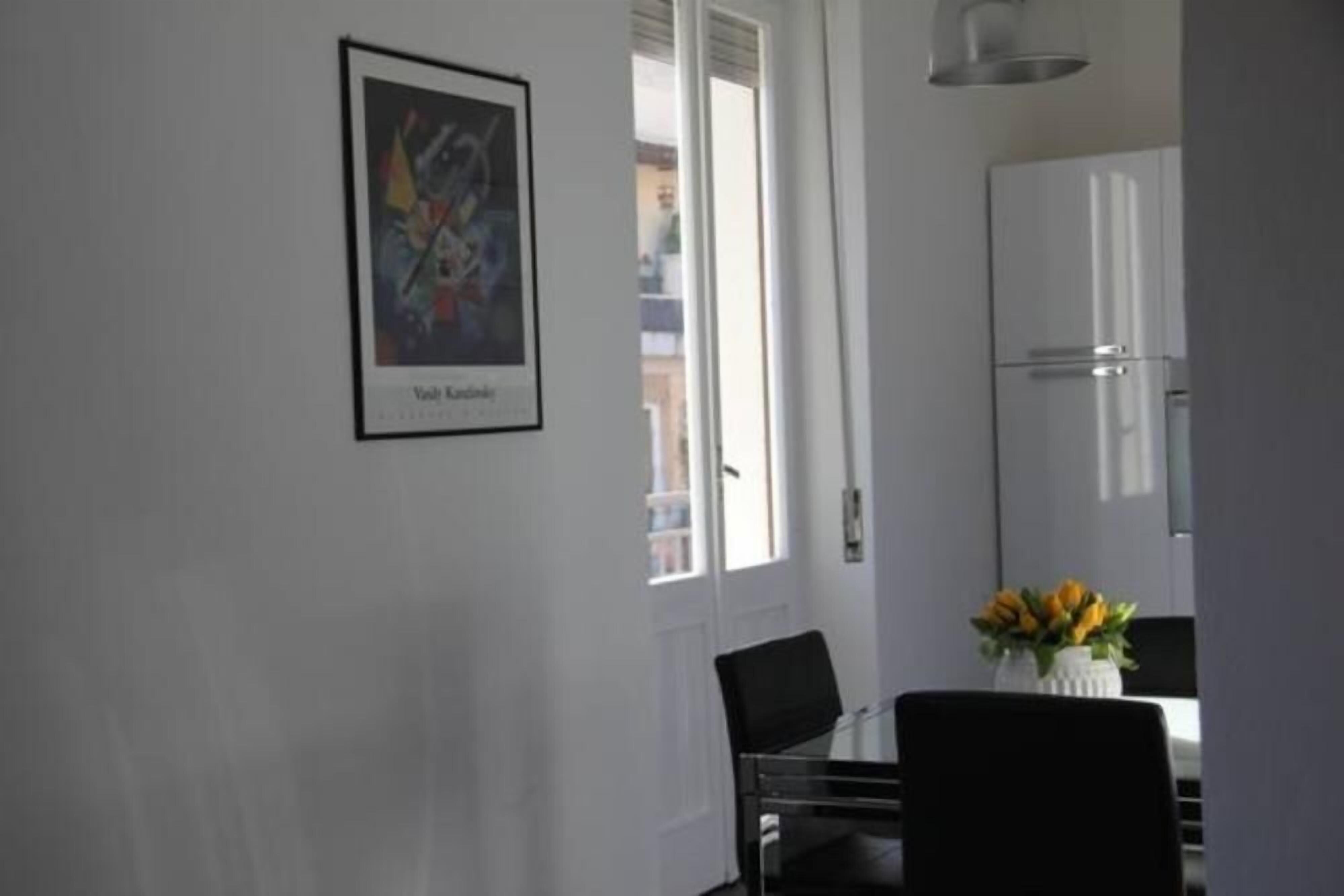 A dining area with a table, chairs, a framed artwork, and a refrigerator.