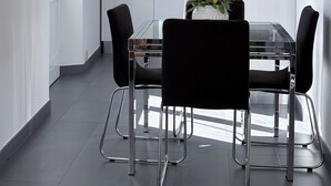 Une cuisine moderne avec des meubles blancs, un four encastré et un coin repas comprenant une table en verre et des chaises noires.