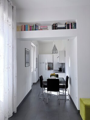A modern kitchen with white cabinets, a dining table with chairs, and a bookshelf above the counter.