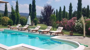 A swimming pool with lounge chairs and a garden with tall trees and flowering plants.