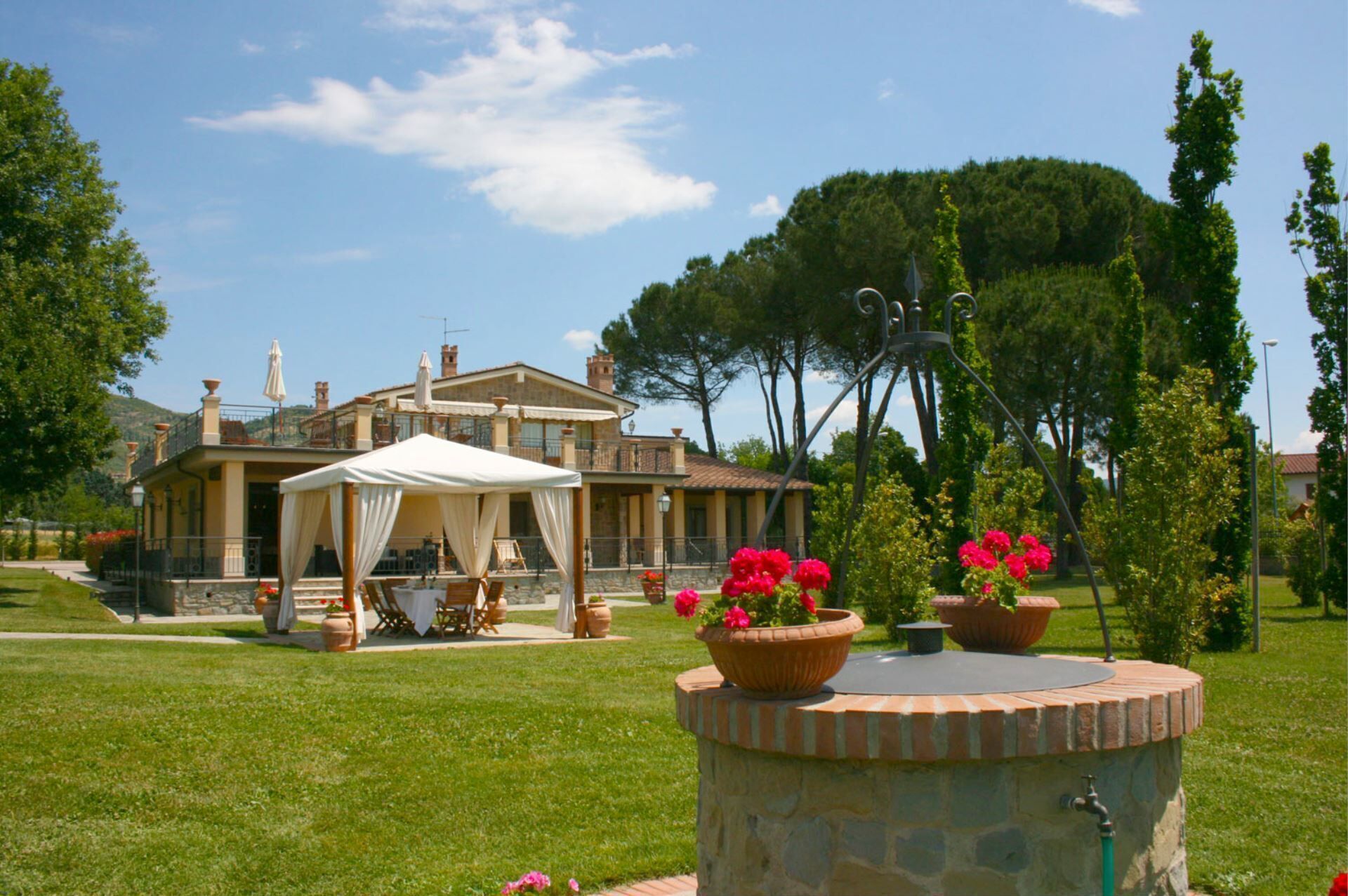 A villa with a covered outdoor seating area, a stone well, and a garden with potted plants.