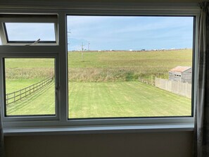 Una ventana con vistas a un campo cubierto de hierba y una valla de madera.