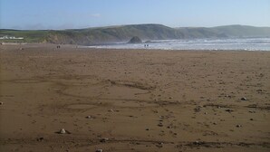 Una extensa playa de arena con rocas dispersas y algunas personas a lo lejos.