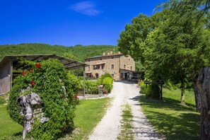 Ein rustikales Steinhaus mit Kiesweg, umgeben von Grün und Bäumen.