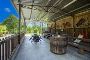 Eine überdachte Terrasse im Freien mit Tischen und Stühlen, einem Holzfass und einer Holzwand mit diversen Gegenständen.