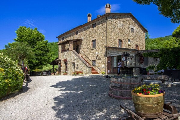 Un bâtiment en pierre avec un escalier menant à l’entrée, une enseigne indiquant un restaurant et un jardinier en premier plan.