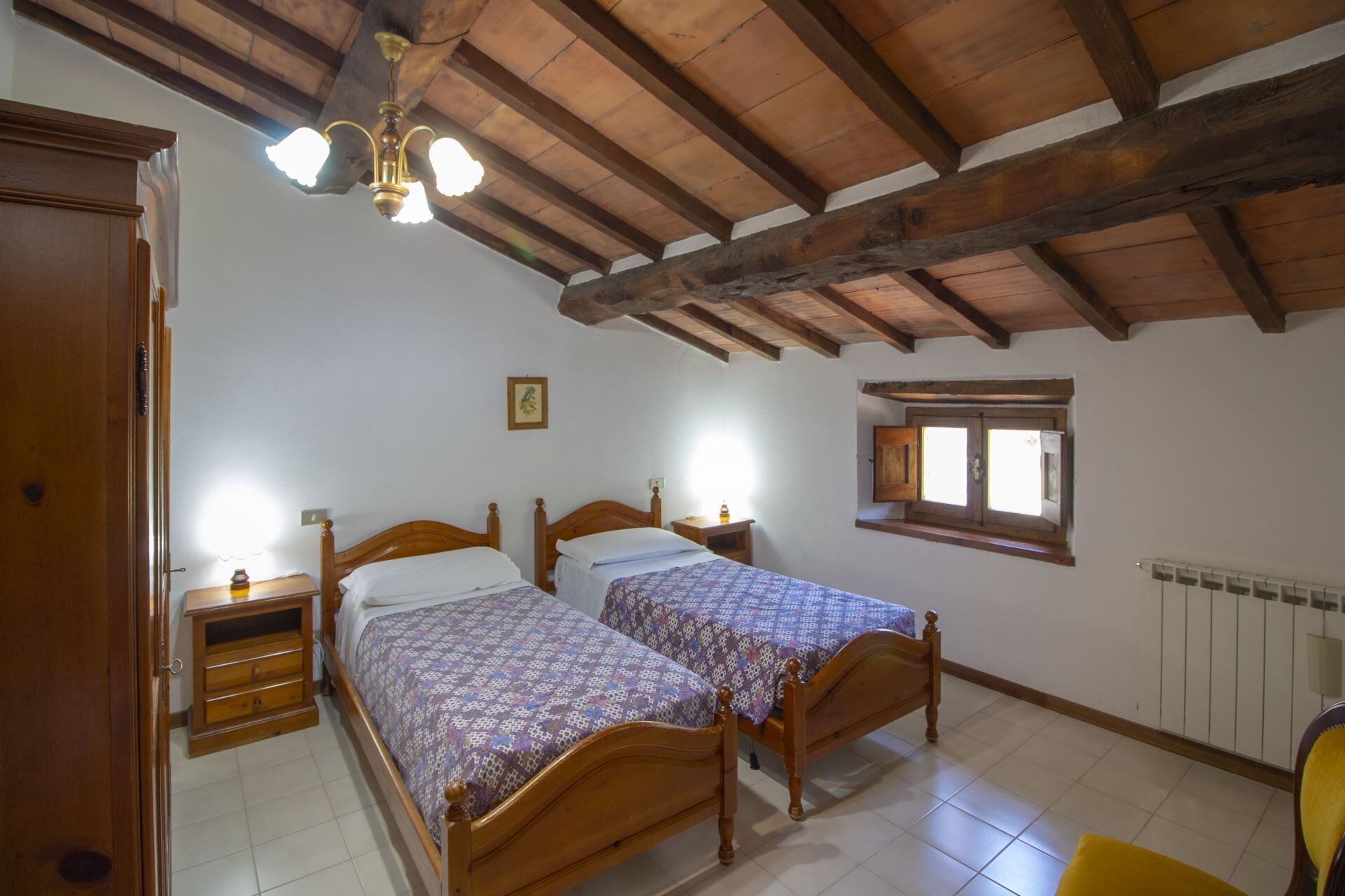 Une chambre avec deux lits en bois, un plafond en bois, une fenêtre et un radiateur.