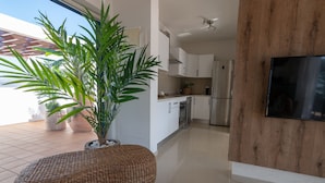 Une cuisine moderne avec des meubles blancs, un réfrigérateur en acier inoxydable et une grande plante en pot.