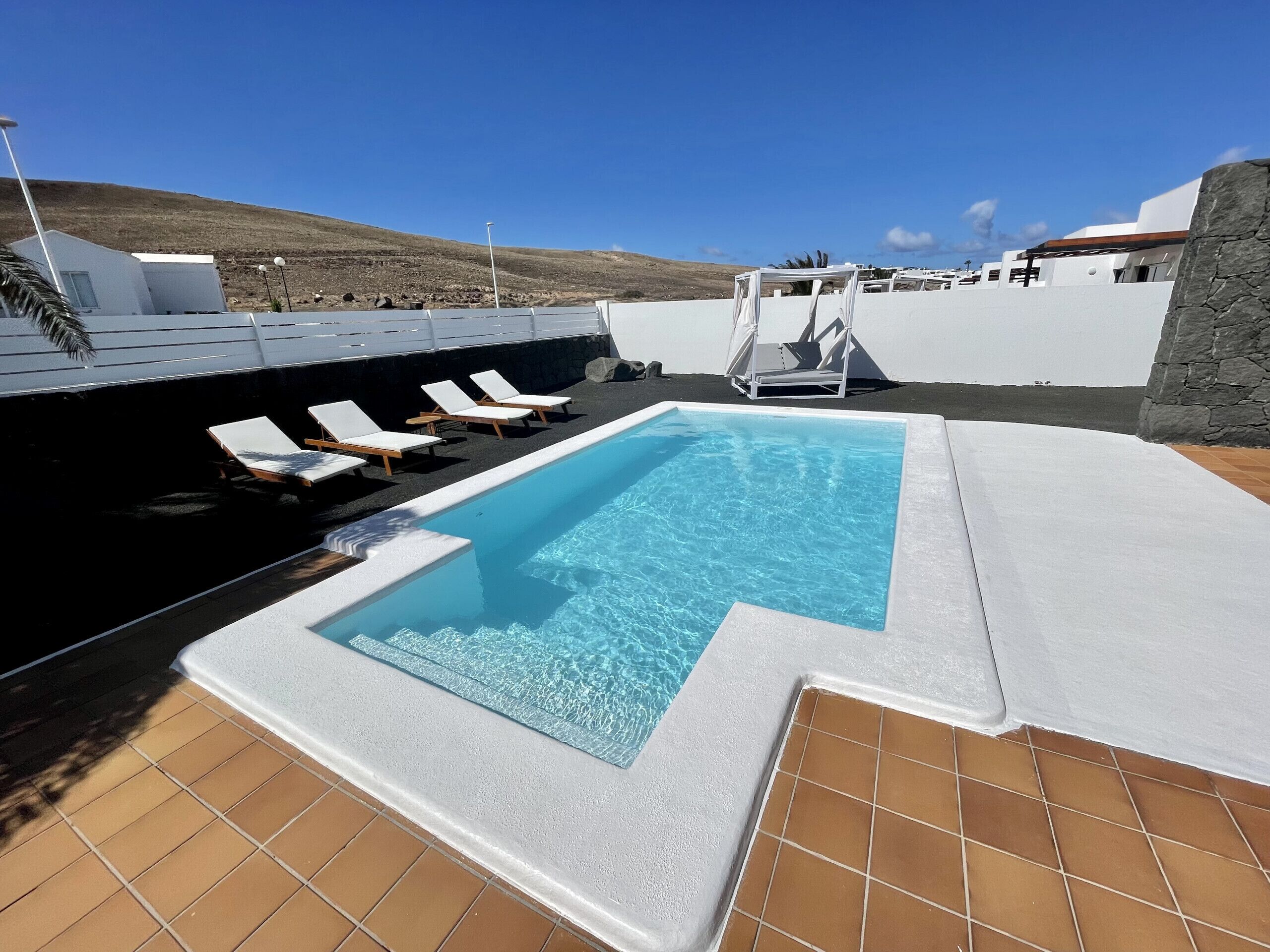 A swimming pool with white lounge chairs and a stone wall.