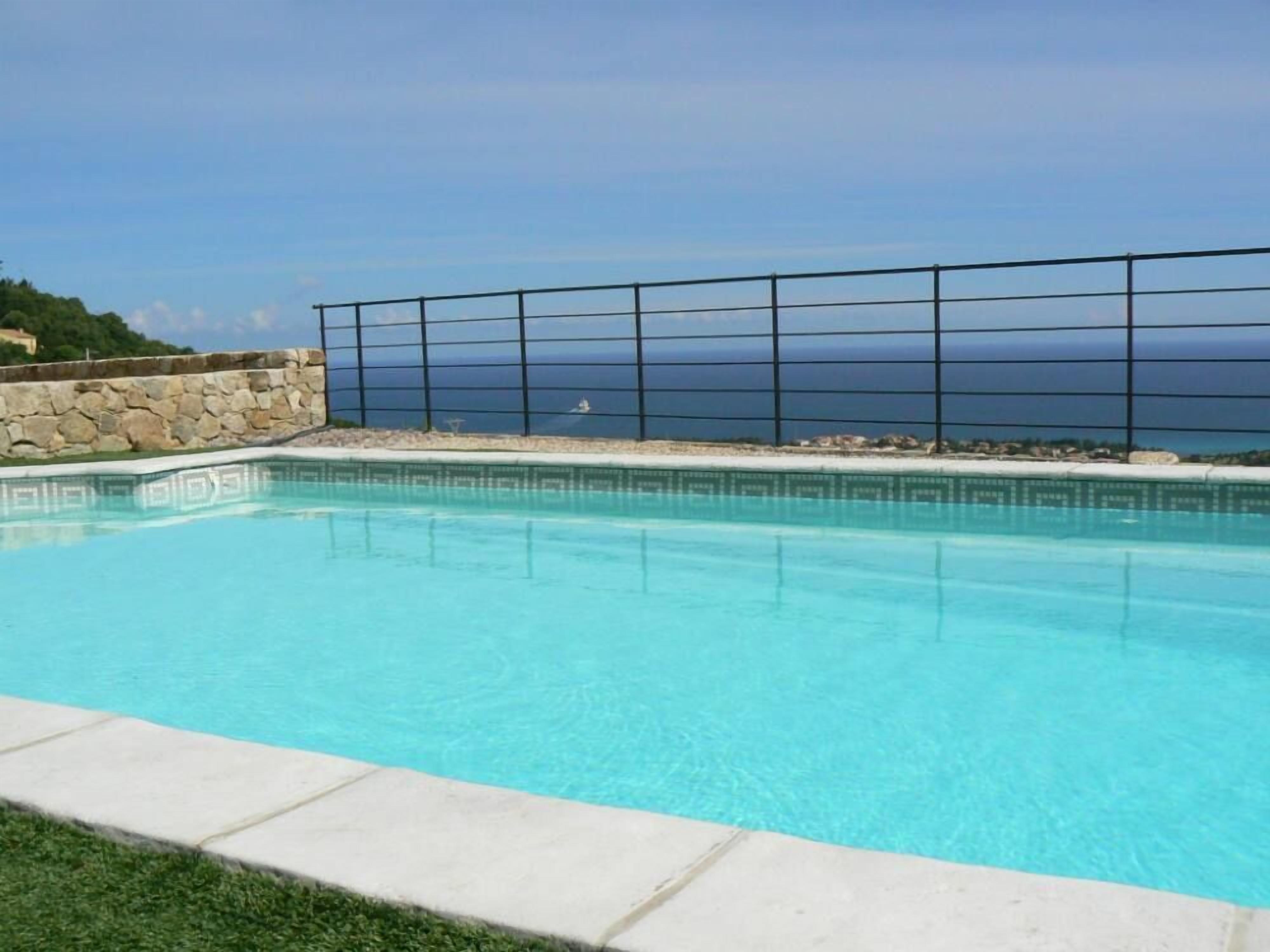 A swimming pool with a stone wall and a metal fence.